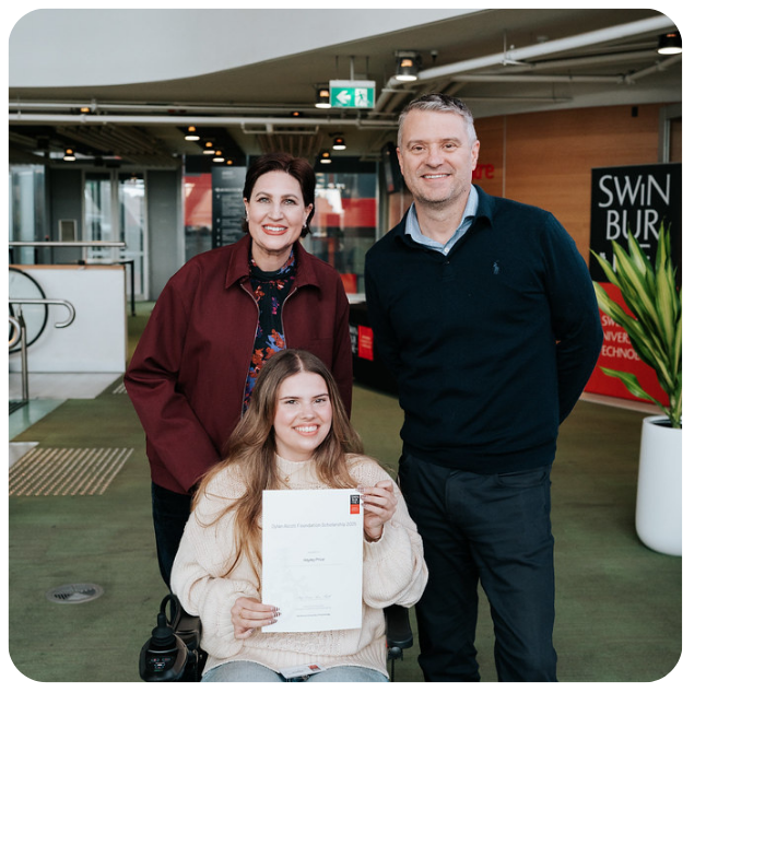 Hayley pictured holding a scholarship certificate in a foyer. She is a wheelchair and parents mum (left) and dad (right) stand behind her smiling to the camera.
