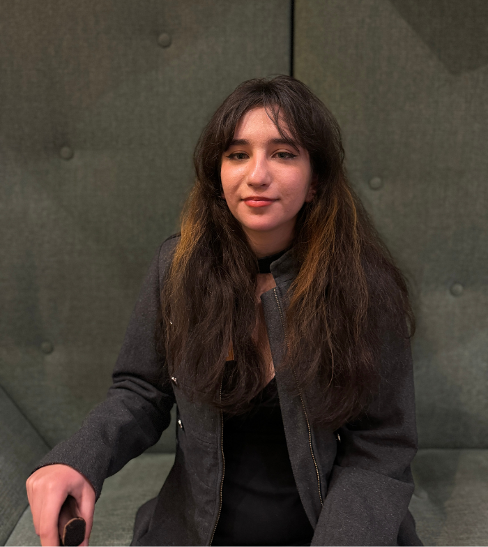 Close up photo of Jamie sitting on a green couch. She smiles to the camera with her long brown hair out, she holds a walking in one hand in front of her.