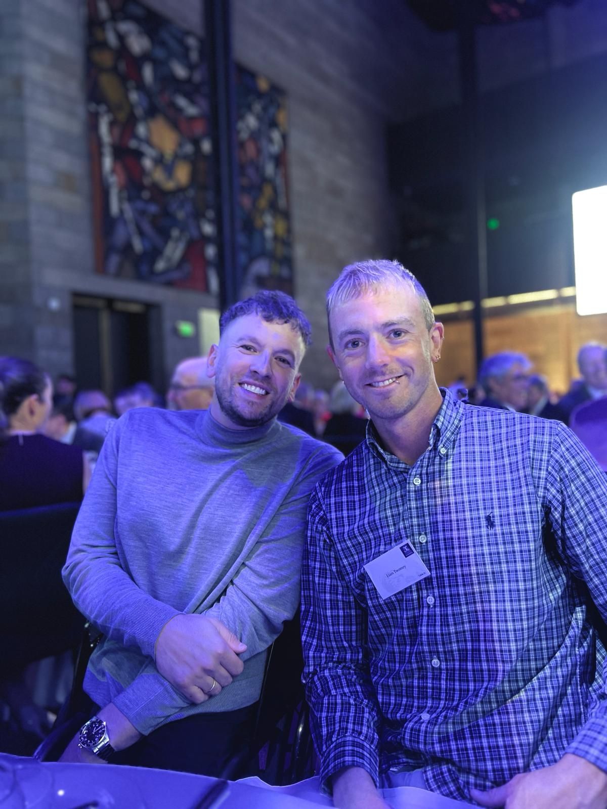 Dylan (left) seated at a table with recipient Liam (right) smiling to camera.