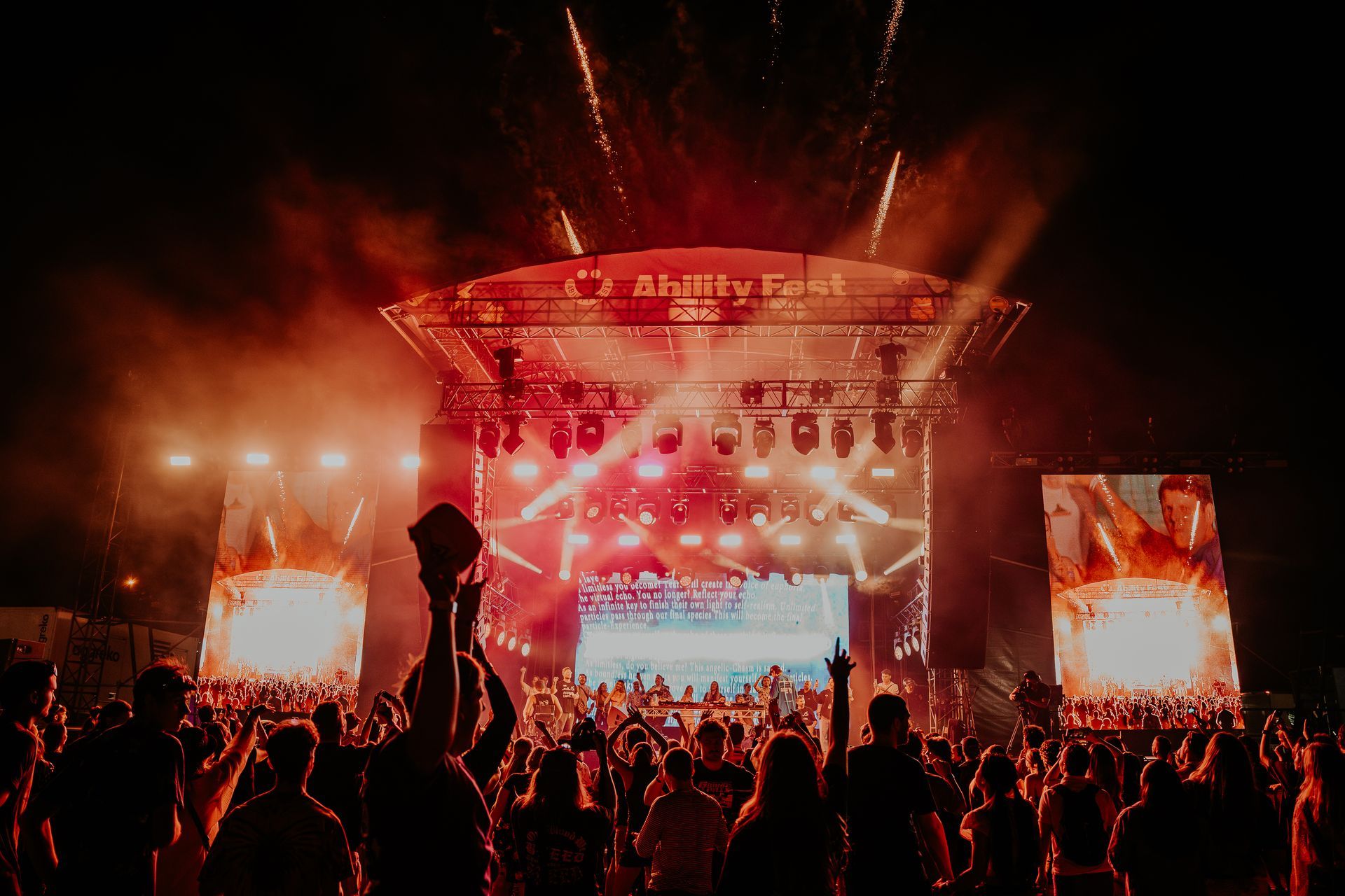 Night time shot of the Ability Fest main stage, bathed in red stage lights with crowd in front.