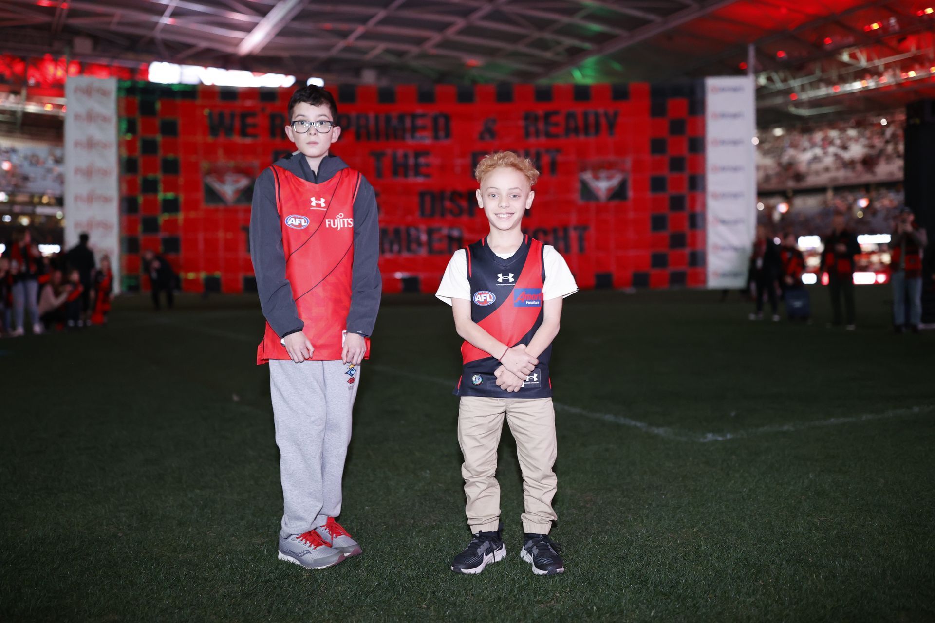 Two junior recipients posing for photo in front of the Essendon banner pre game.