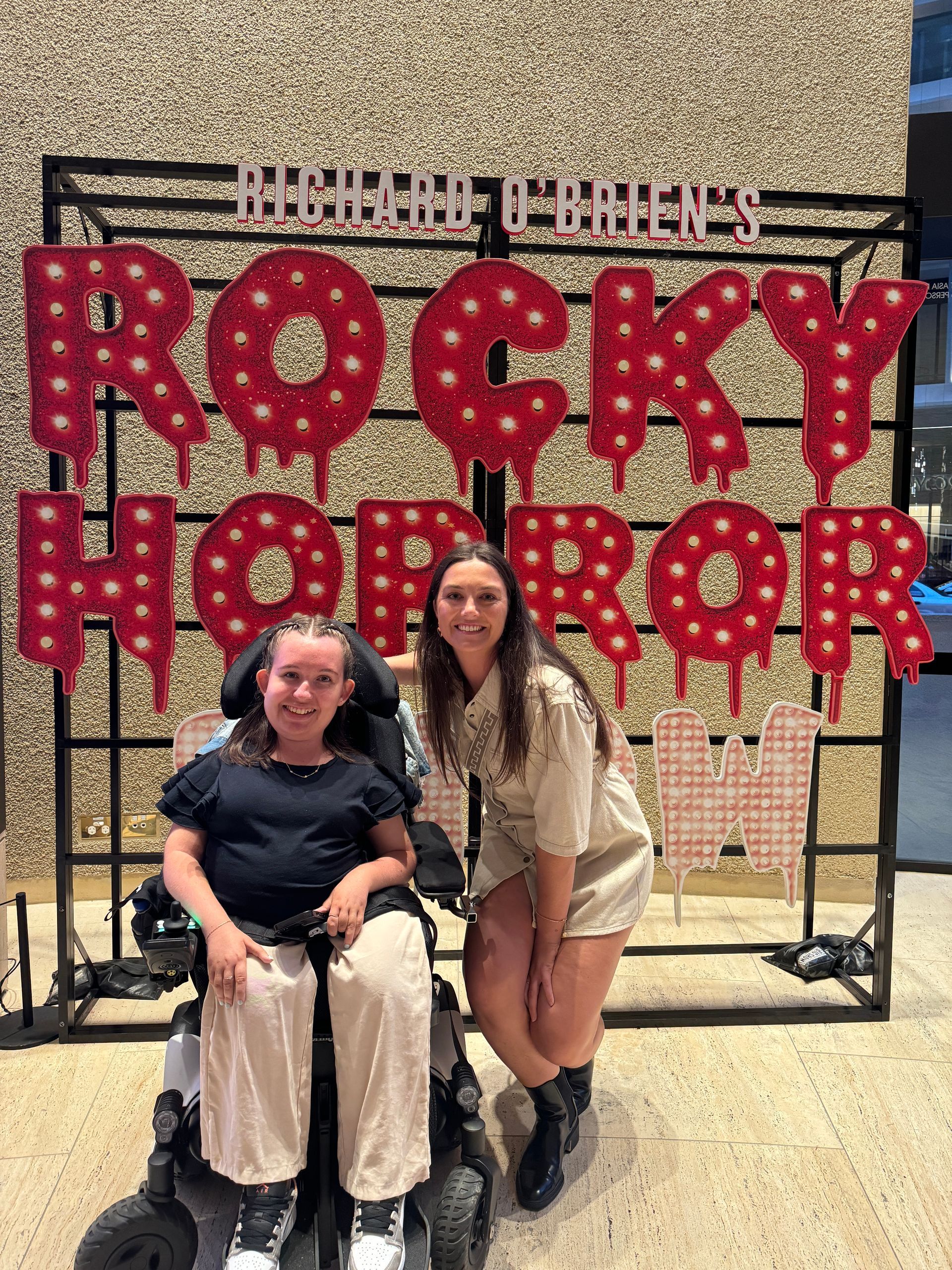 Jamieson (left) and DAF member Stef (right) pose for the camera in front of the red and white Rocky Horror sign that reads - Richard O'Brien's Rocky Horror Show.