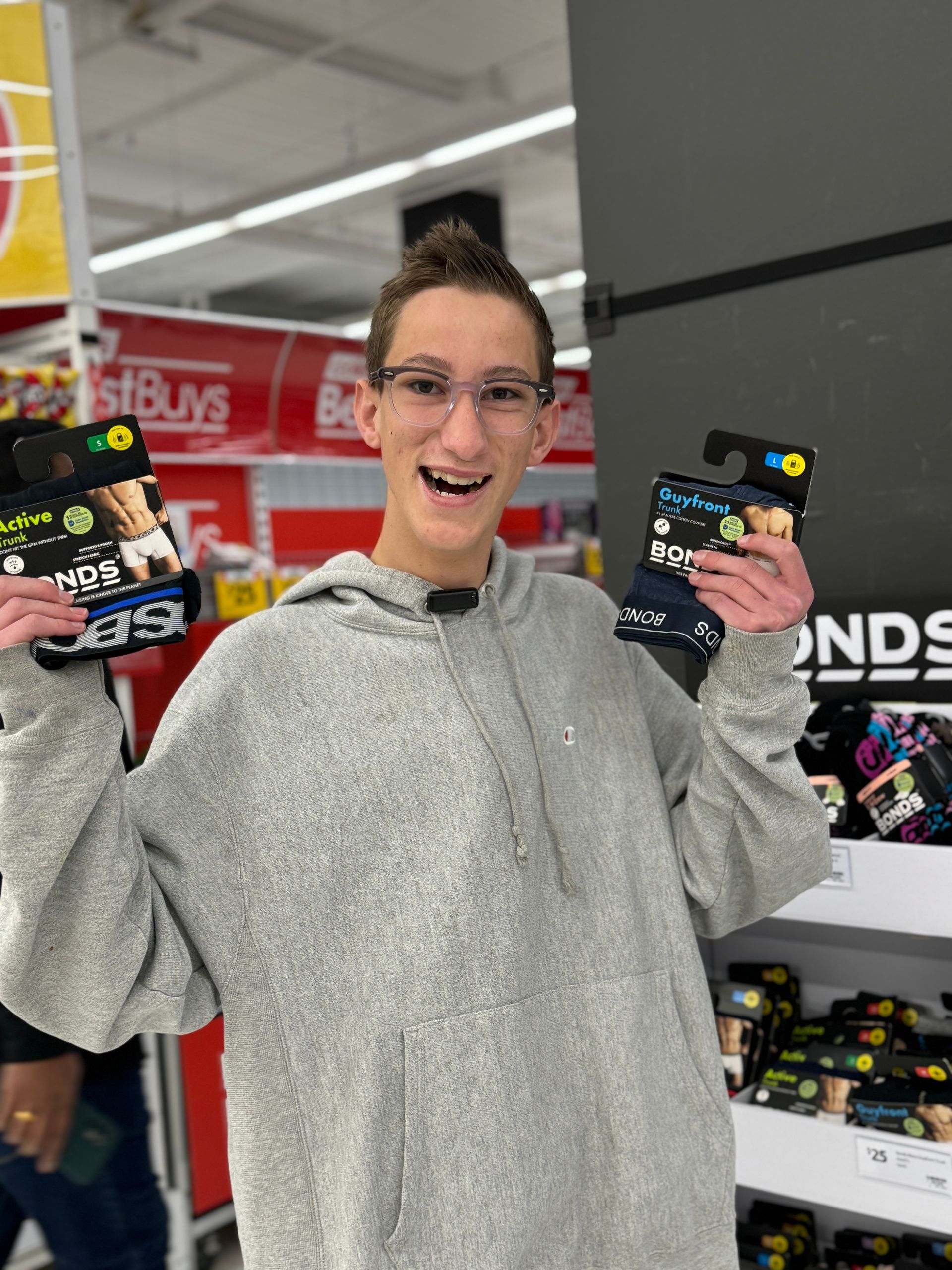 Recipient Sam, holds Bonds undies in both hands smiling to camera. He stands in store at Coles in front of the Bonds and Dylan Alcott Foundation branded product stand.