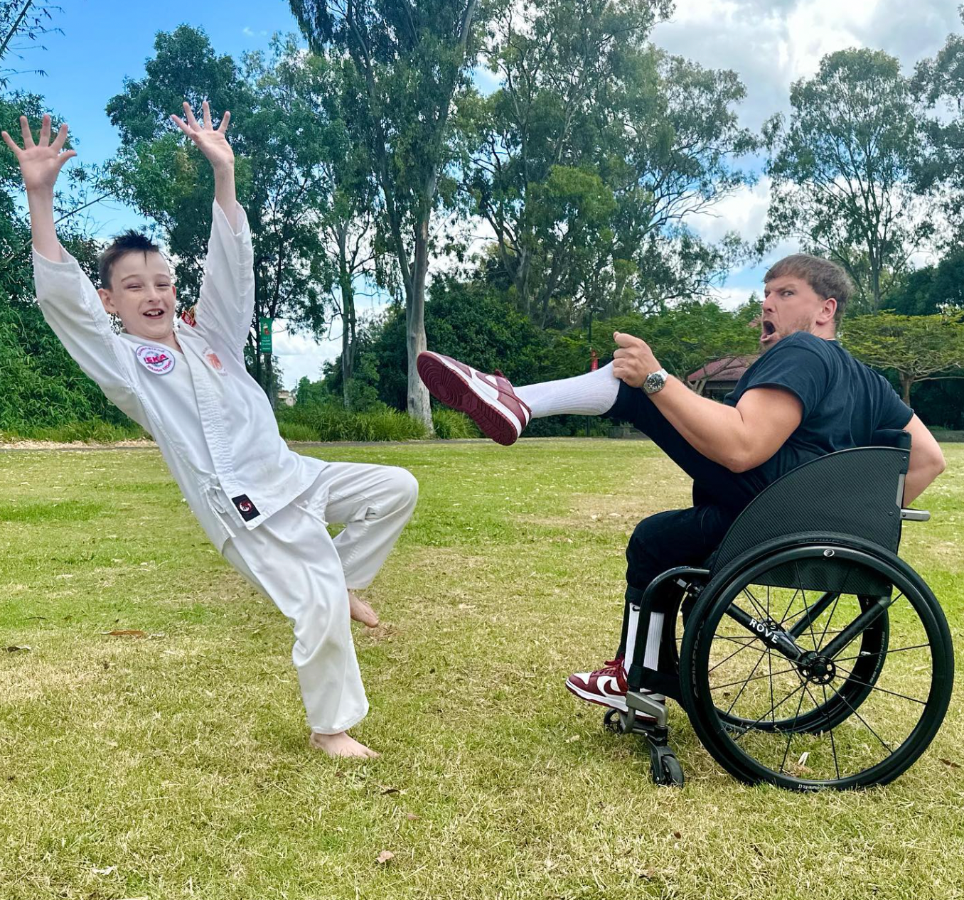 Recipient Jasper (left) wears karate white uniform. He has his hands raised in falling over motion, whilst Dylan (right) holds his leg pretending to karate kick Jasper.