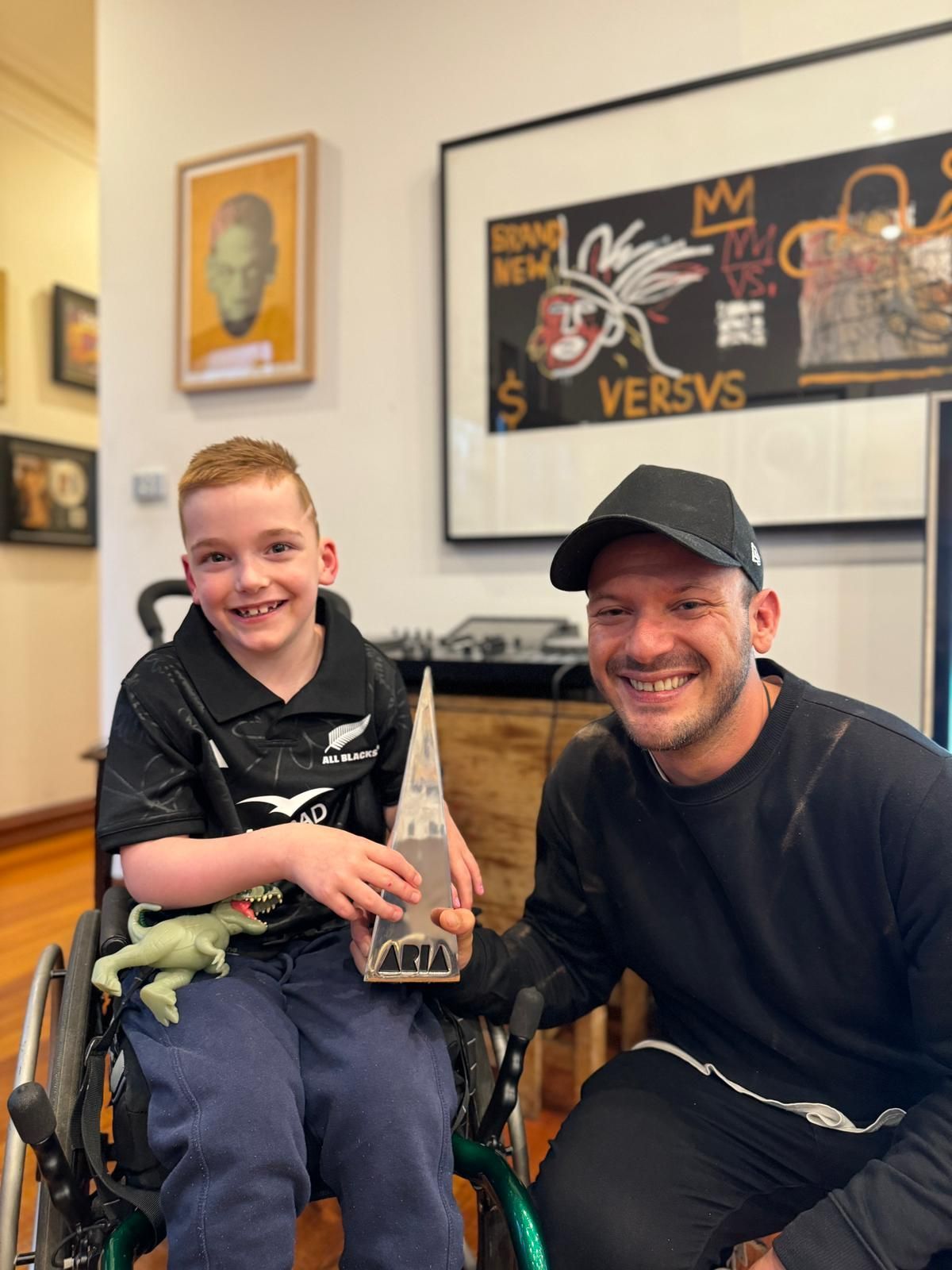 Jaxson pictured in his wheelchair (left) with rap mentor Sean (right), posing for a photo holding an ARIA award.