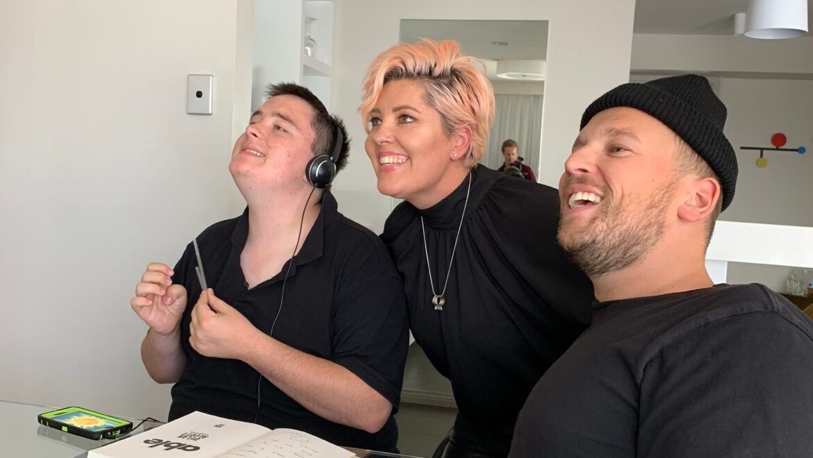 Side photo of Paddy (left) wearing headphones with his mum (middle) and Dylan (right) smiling.