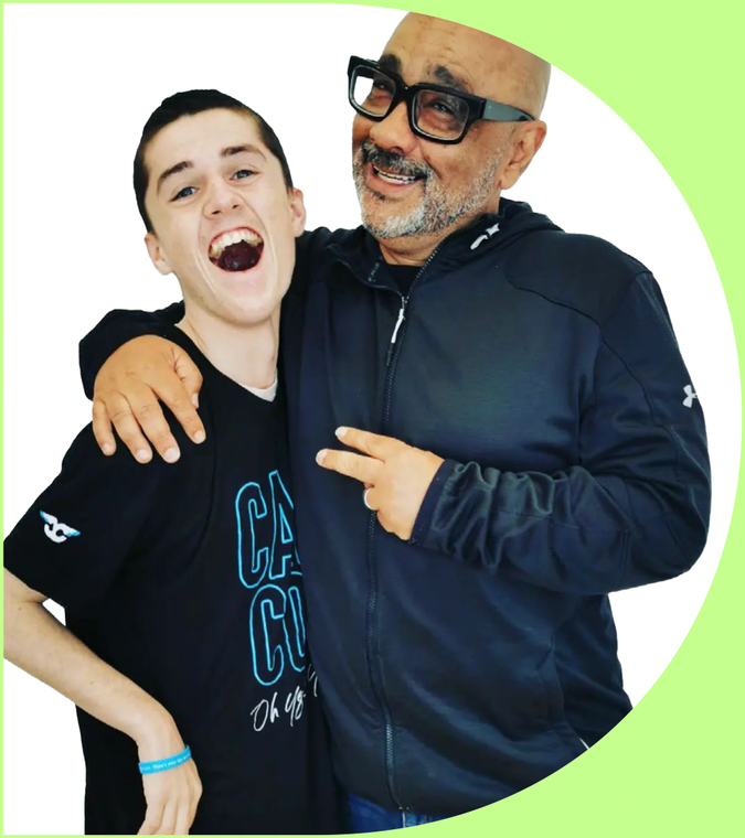 Recipient Cooper (left) and mentor (right) embracing with smiles at the camera. Their photo fills a large white letter D. 
