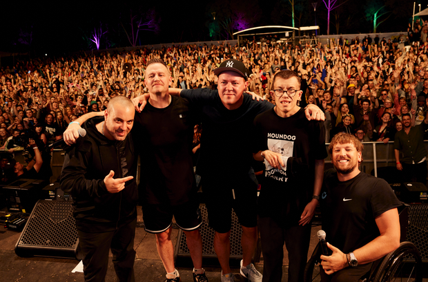Hilltop Hoods (left), recipient Harry Brown (middle) and Dylan (right), posing for photo on stage at Ability Fest with large crowd in the background.