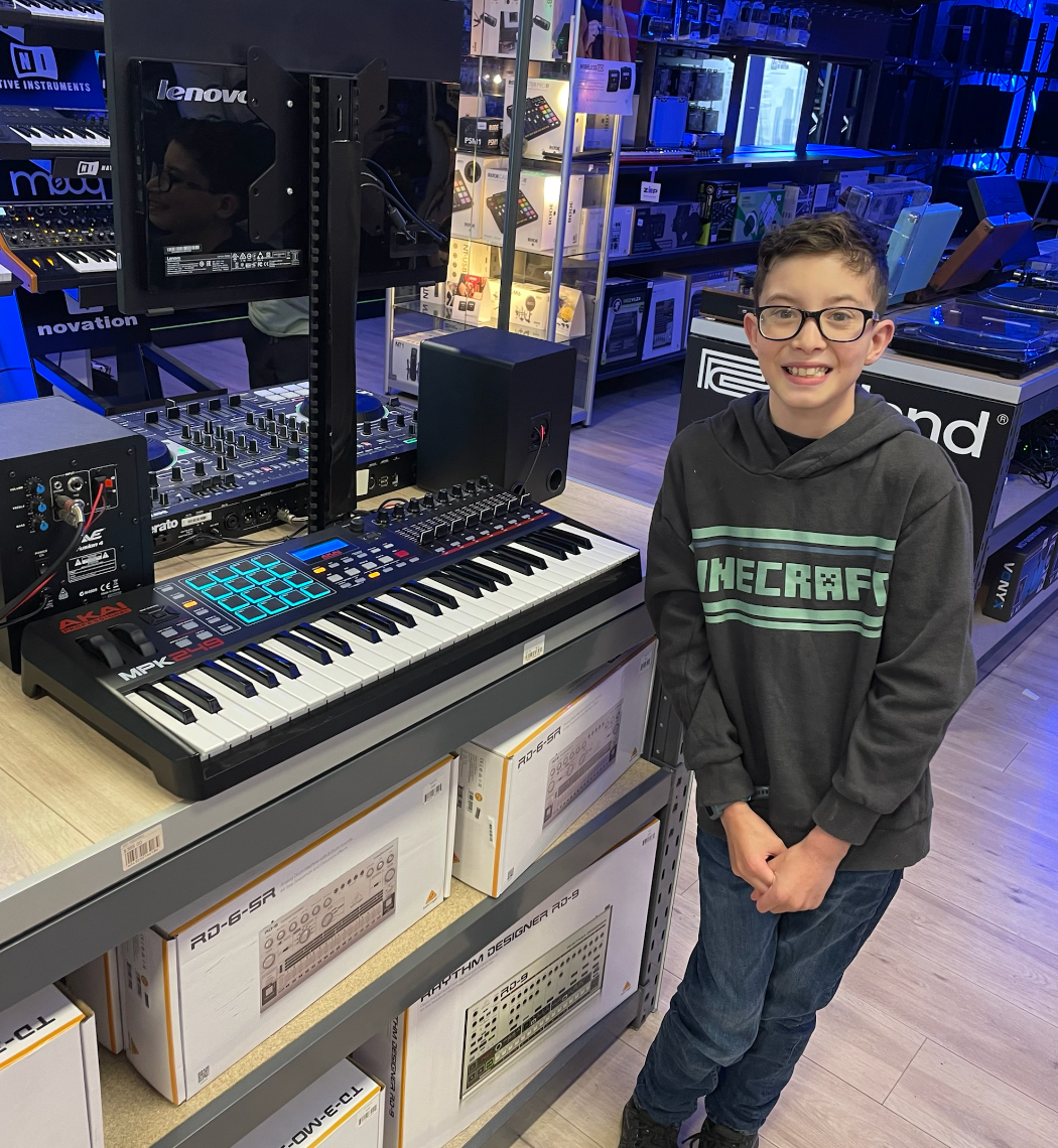 Recipient Nathan stands next to a keyboard in a music shop, smiling to camera.