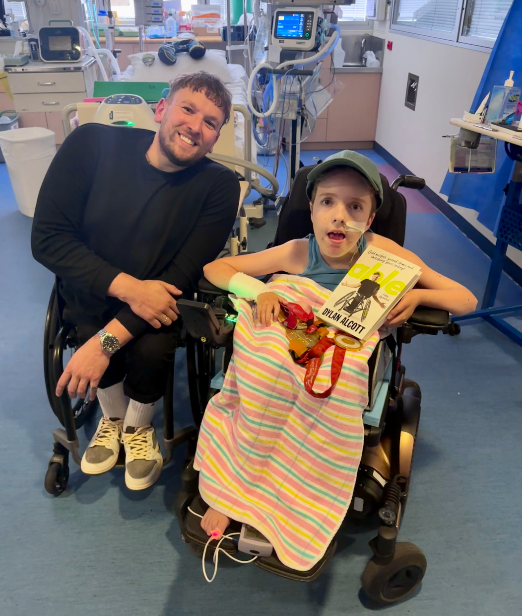 Dylan (left) in hospital with recipient Charlie (right). Both are wheelchair users and Charlie holds Paralympic medals and Dylan's book.