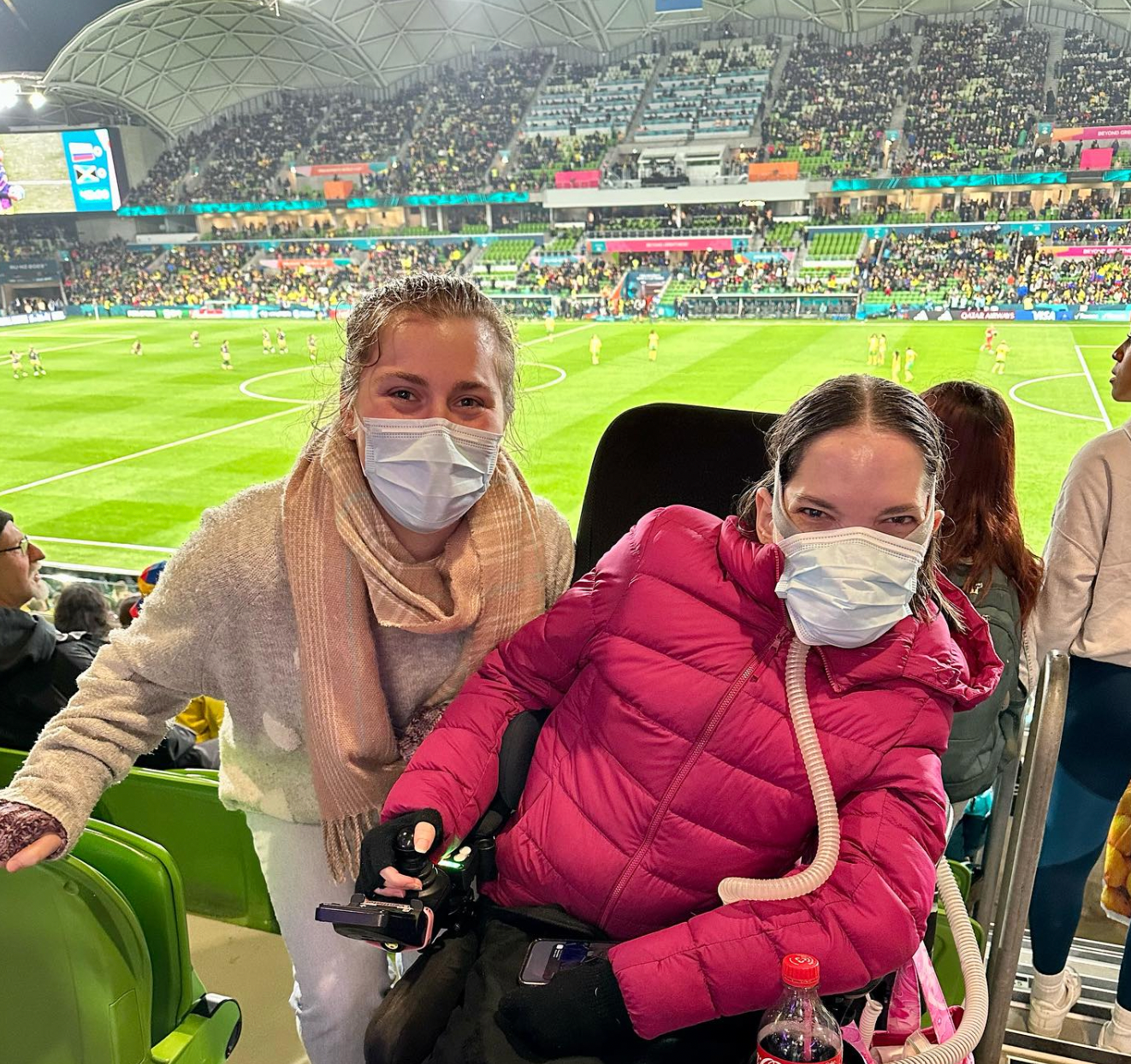 Tahlia (left) and DAF recipient, Rebecca (right) in the stands at the FIFA Women’s World Cup. The green football pitch and crowd can be seen in the background.