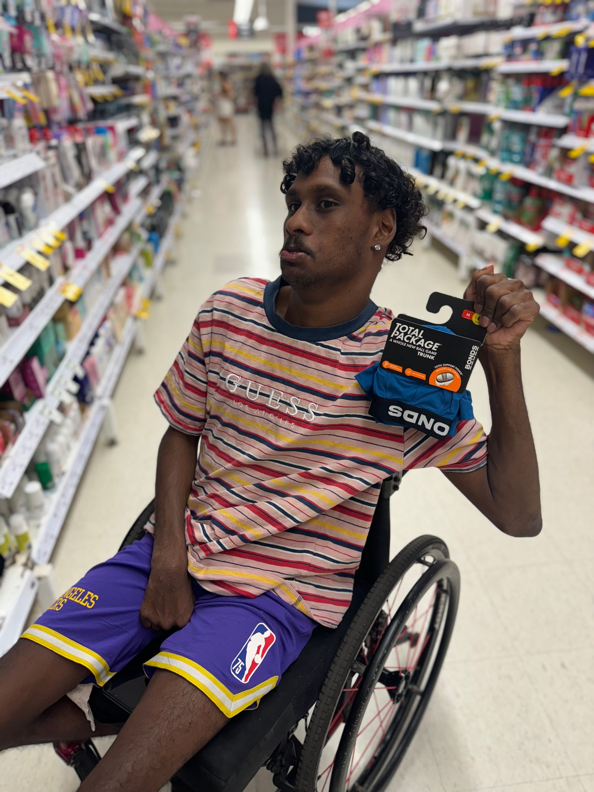 Recipient Thomas is a wheelchair user. He poses for a photo in aisle at Coles supermarket holding up Bonds undies in his right hand.