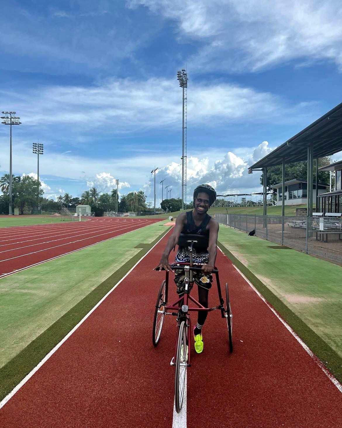 Located on an athletics track, Thomas smiles at the camera whilst seated on his frame runner that has 3 large wheels