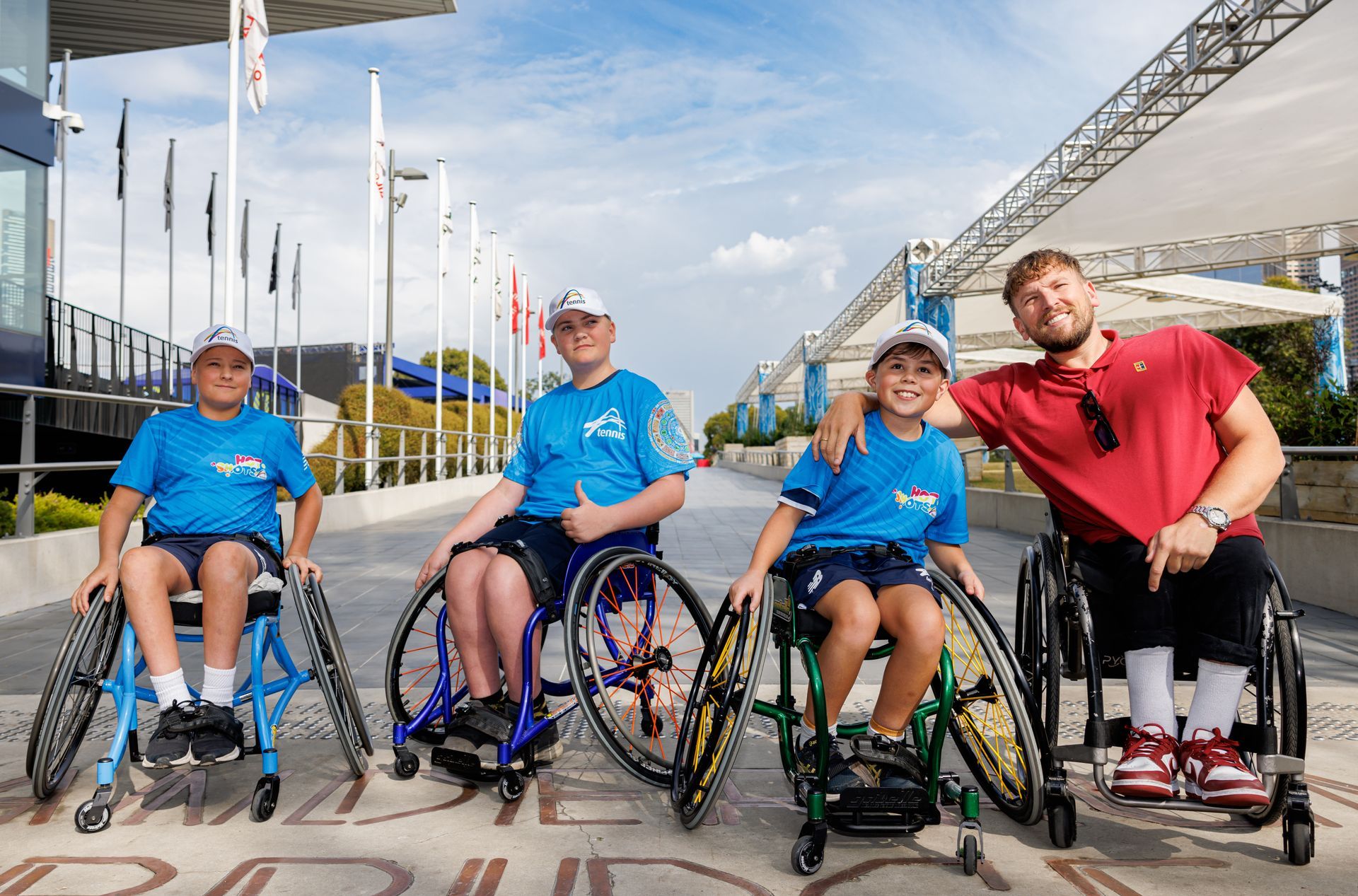 Three junior wheelchair tennis players (left) with Dylan (right) smiling to camera at the AO.