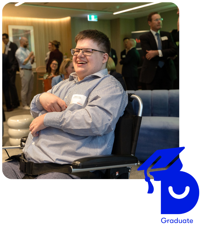 Side profile photo of Cameron who is a wheelchair user. He wears a dress shirt and a name badge and is mid laugh. The background is a blurred audience of a keynote. The dark blue capital D of the DAF logo has a smiley cut out and wears a dark blue graduation hat with the words 'Graduate' underneath. This logo is placed at the bottom right hand side, slightly covering the photo.