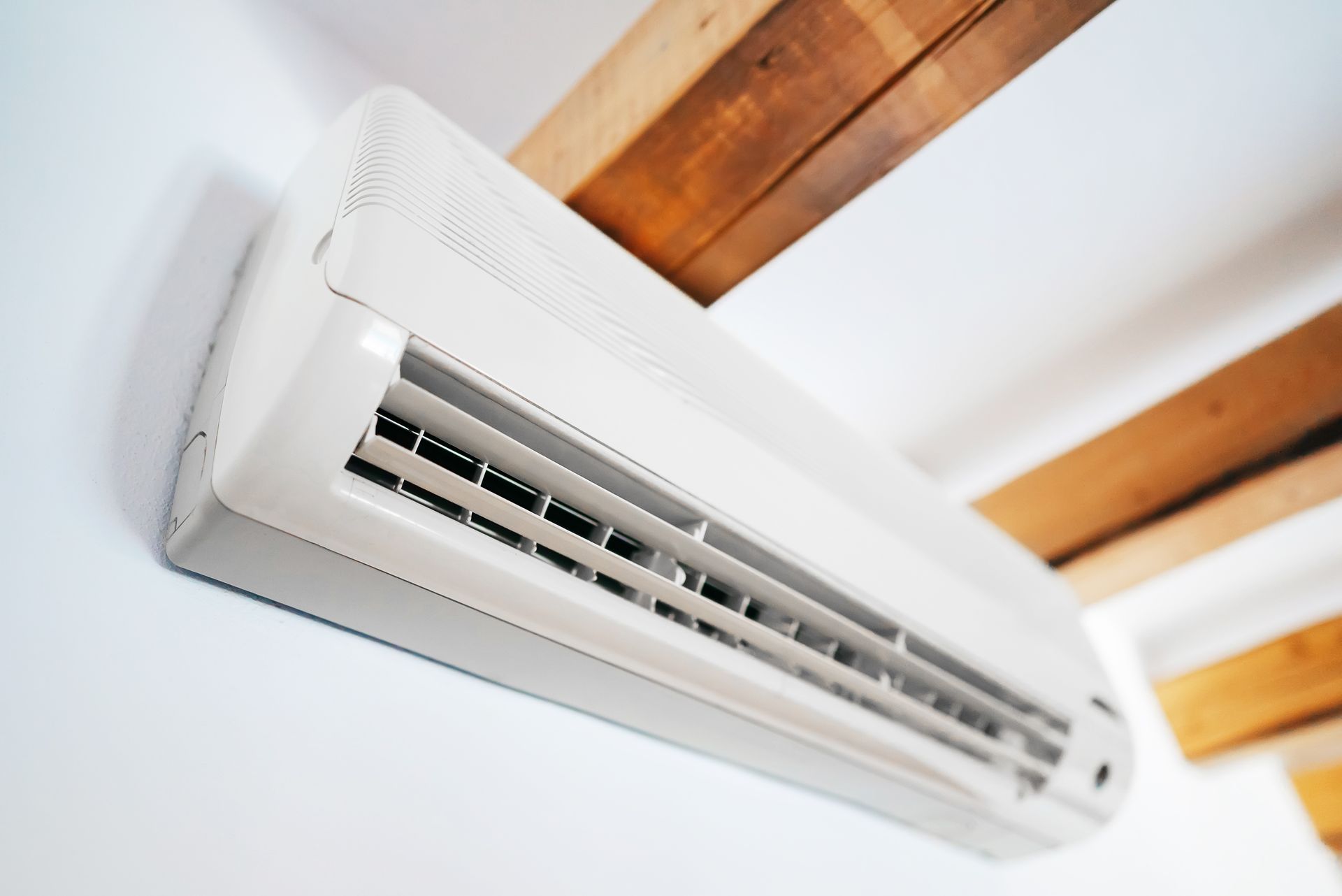 White air conditioning unit mounted on a white wall, wooden beam overhead.