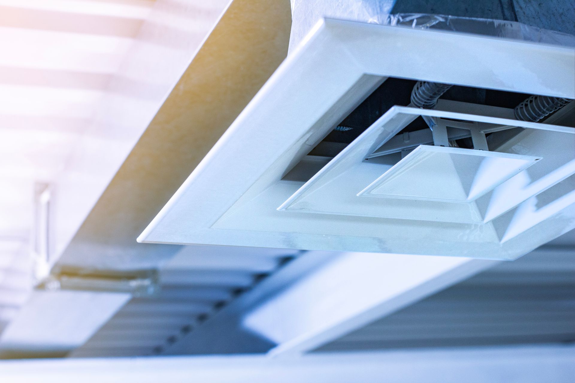 White air vent on a ceiling with a metal duct, inside a building.