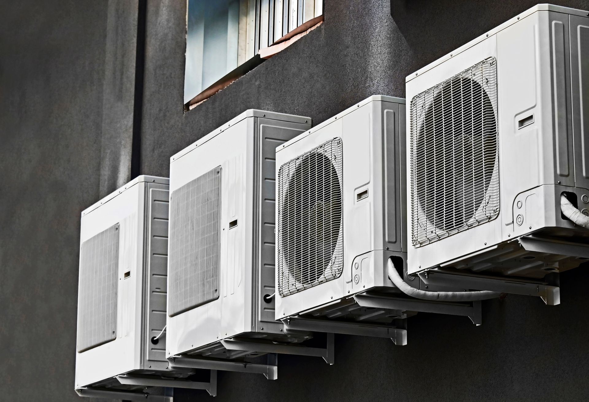 White air conditioning units mounted on a dark gray building exterior.
