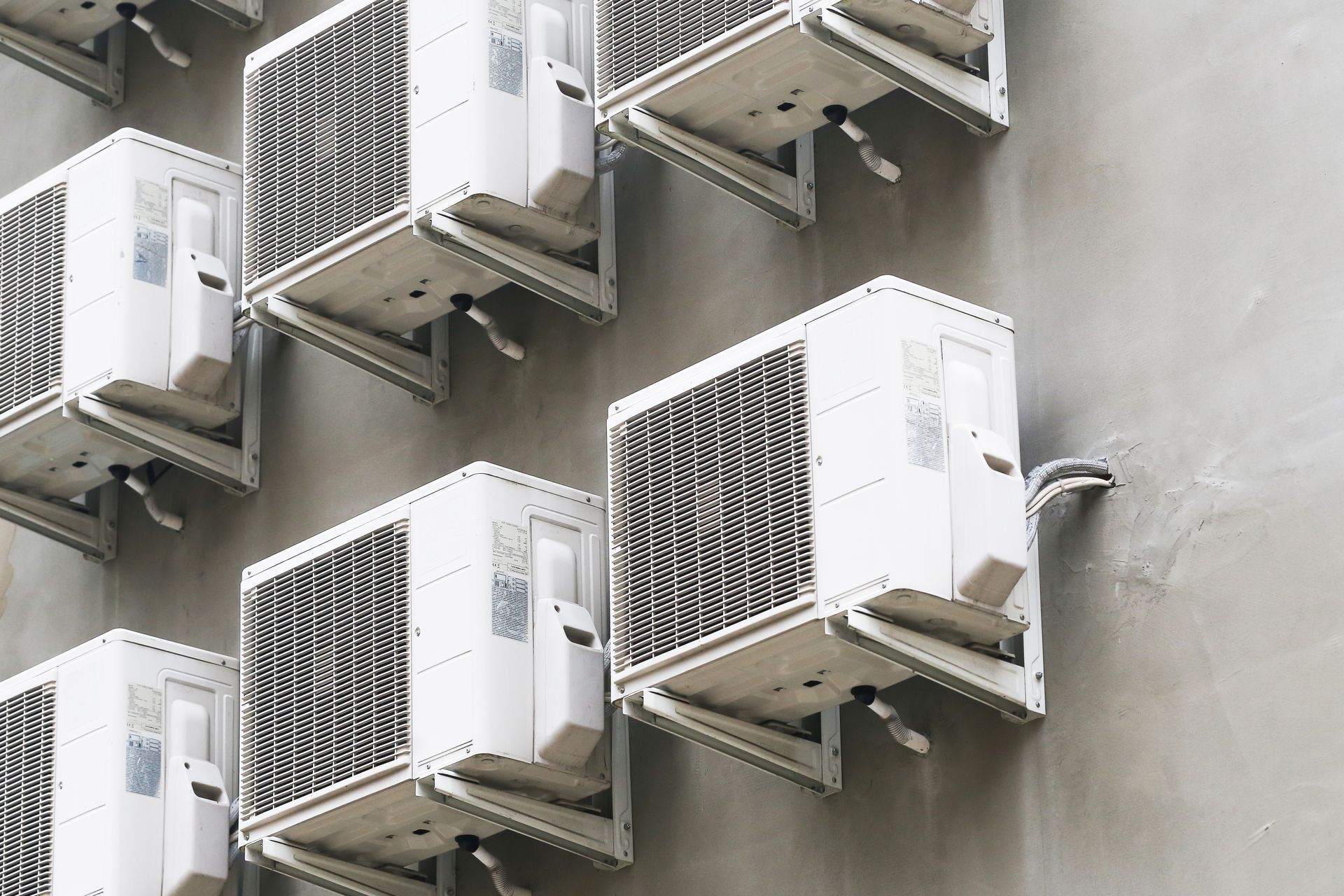 Rows of white air conditioning units mounted on a gray wall.