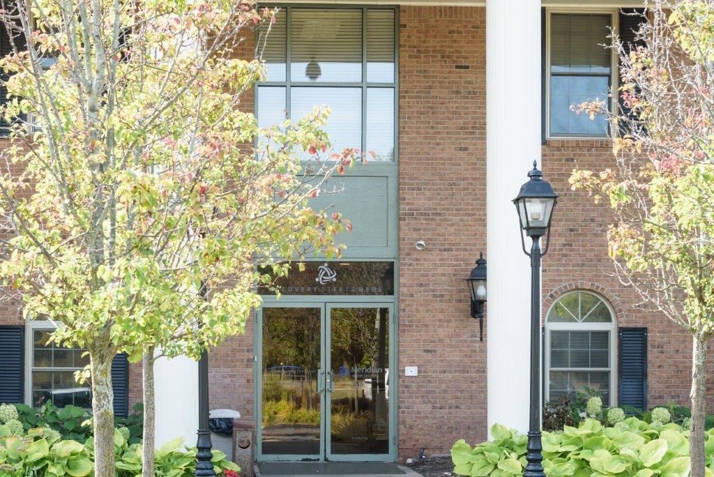 Brick building entrance with glass doors, large window, street lamp, and trees.