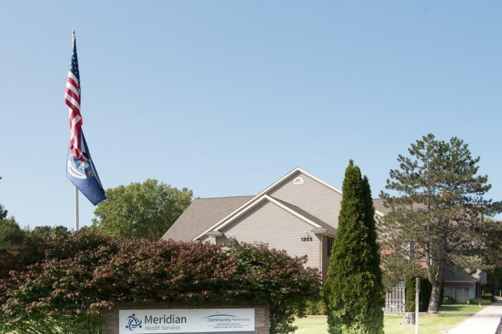 American and state flags fly in front of a building with a Meridian Behavioral Health sign.