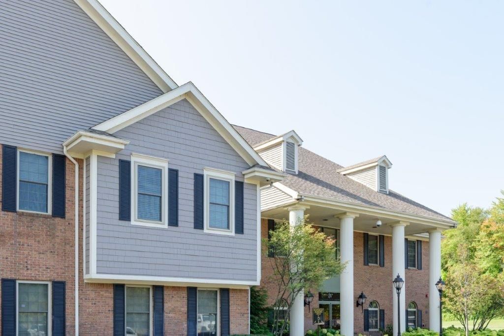 Large brick house with gray roof, pillars, and multiple windows.