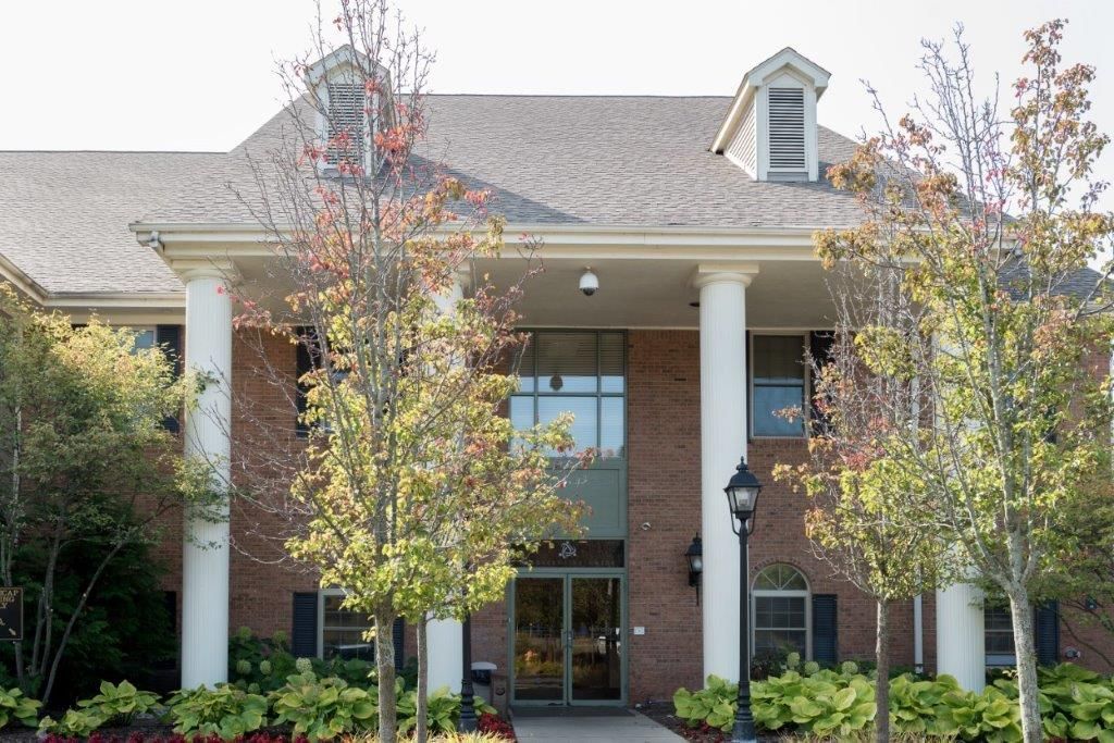 Brick building with white columns and dormers; trees and landscaping in front.