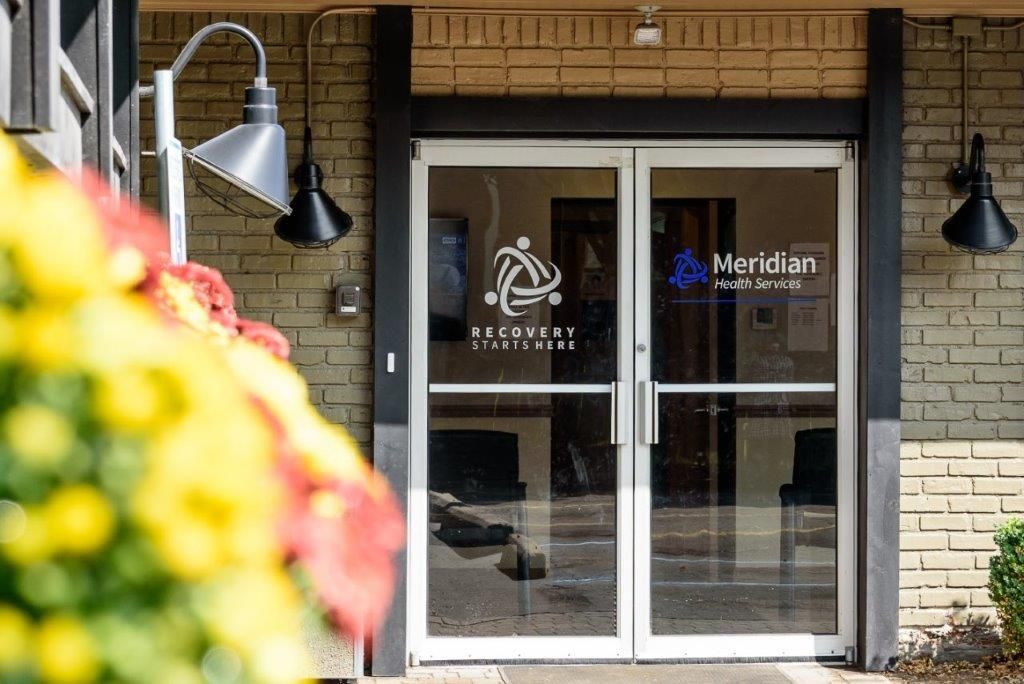 Entrance doors with Meridian Health logo and outdoor lights and flowers.
