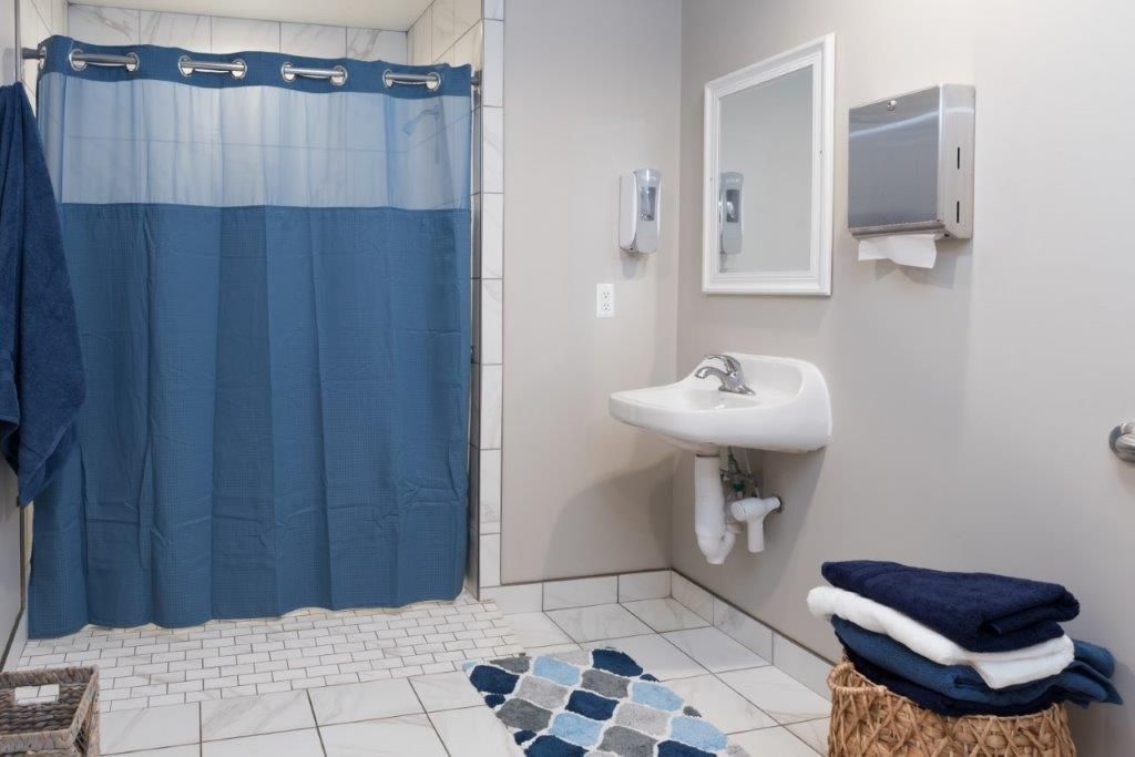 Accessible bathroom with a blue shower curtain, sink, towels, and rug.