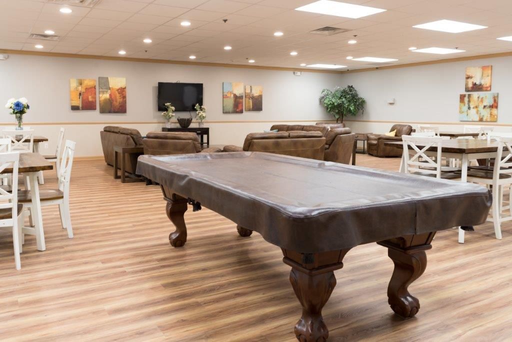 A large room with a pool table covered in a brown cloth, seating, and a TV.