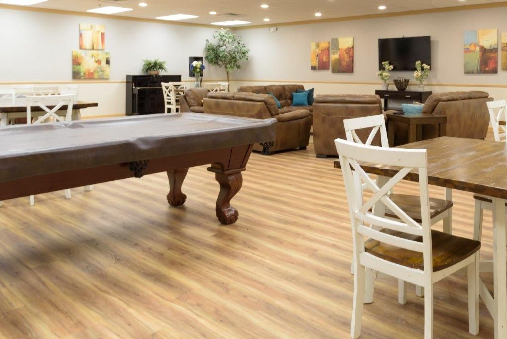 Spacious community room with pool table, couches, tables, and artwork on the walls.