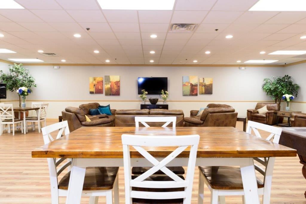 Spacious lounge area with wood tables and white chairs, brown couches, and a TV on the wall.