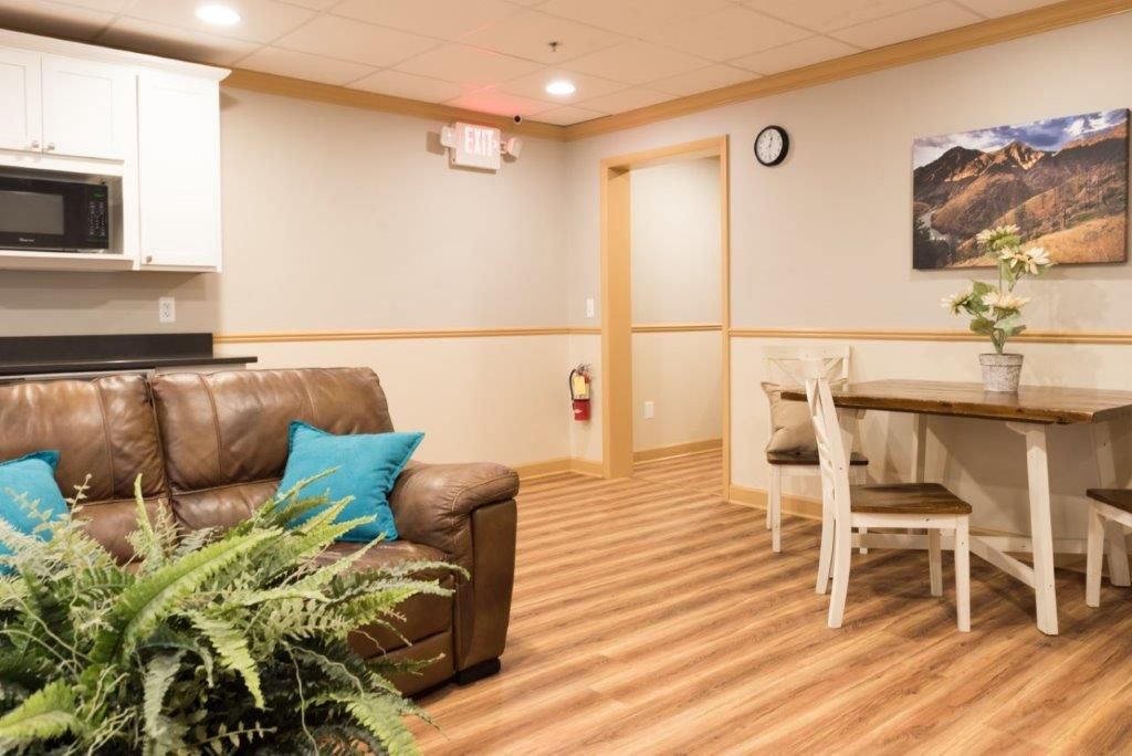 Cozy living area with brown leather couch, small dining table, microwave, and artwork on the wall.