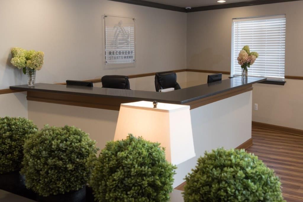 Reception desk with black countertop, three black chairs, and potted greenery.