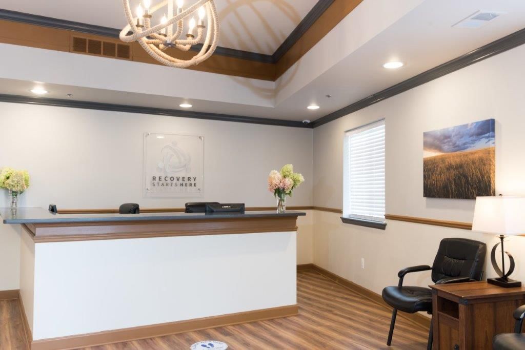 Reception area with a desk, seating, flowers, artwork, and overhead lighting.