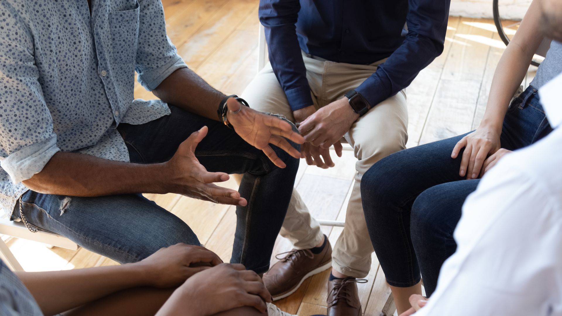 Group of people seated in a circle, leaning in with hands stacked in the center during a team discussion