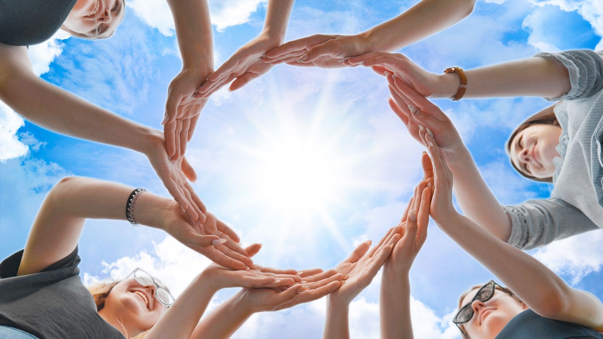 Hands forming a heart around bright sunlight in a blue sky
