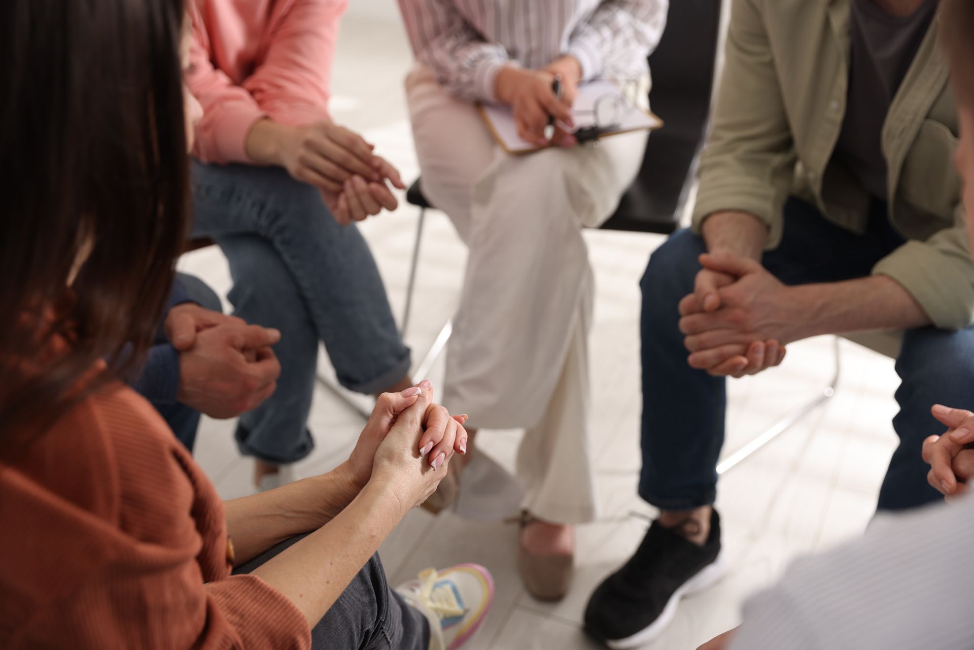 People in a circle, hands clasped, at a support group session.