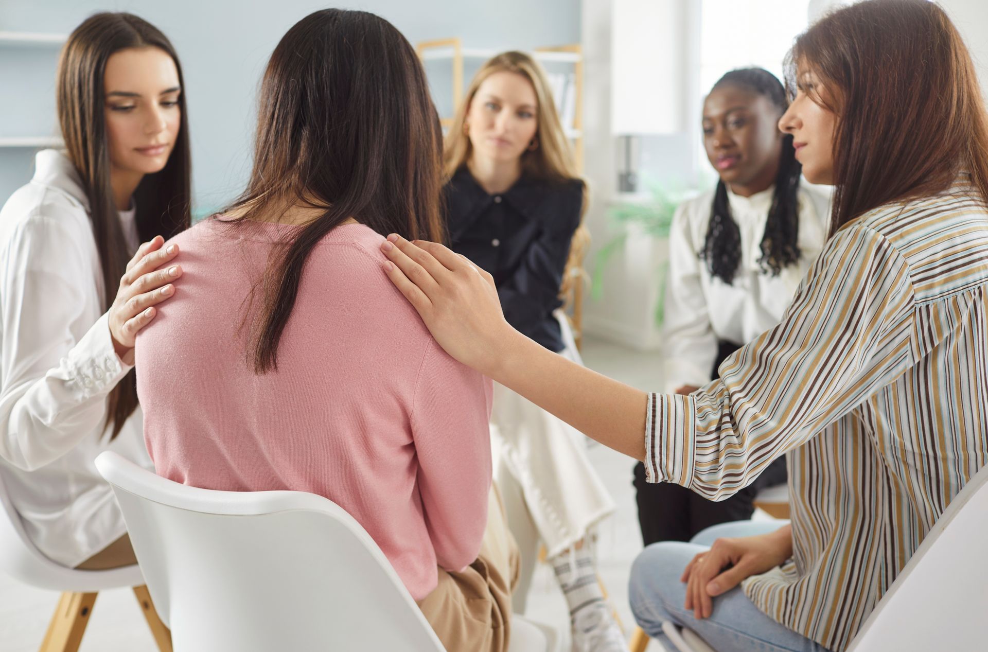 Small group sitting in a circle, one person comforting another during a support session