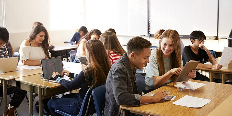 A group of students are sitting at desks in a classroom using laptops.