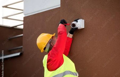 A man is installing a security camera on the side of a building.