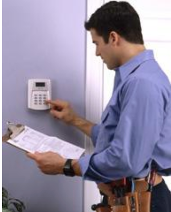 A man is working on a security system while holding a clipboard.