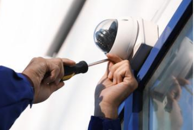 A man is fixing a security camera with a screwdriver.