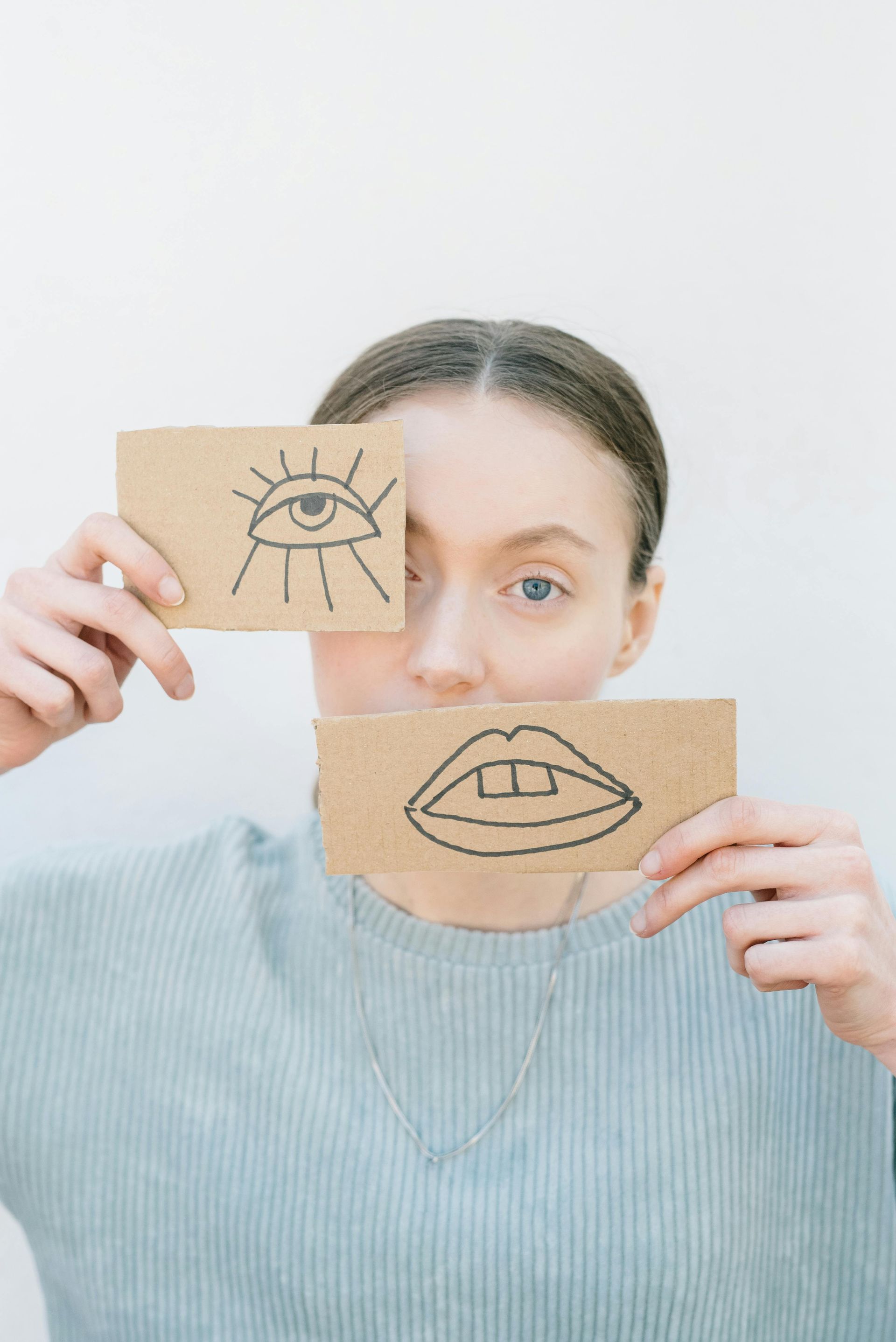 A woman is holding a card with a drawing of an eye and a mouth on it.