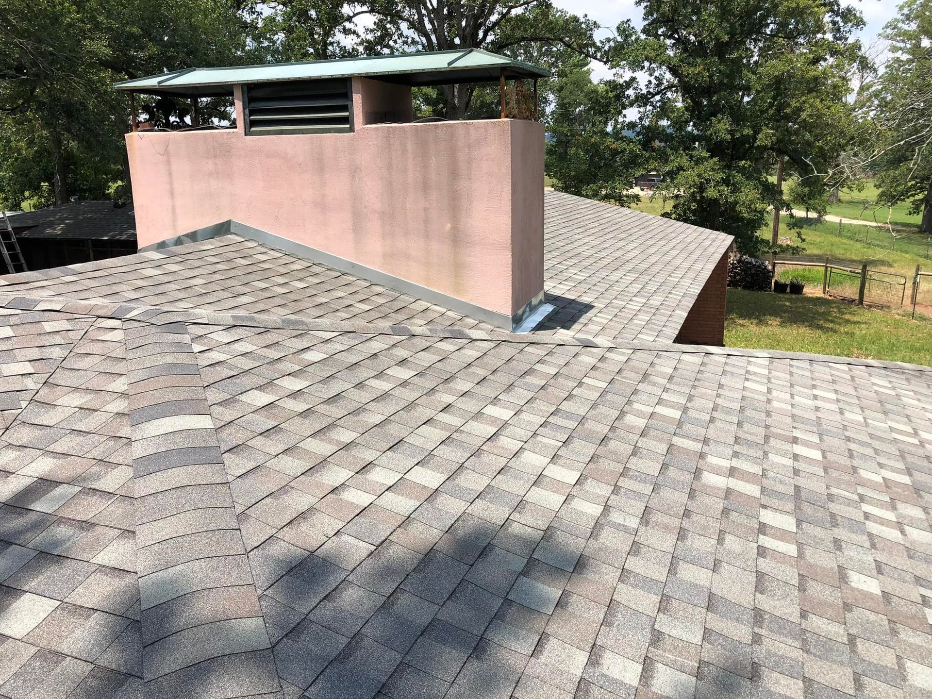 A roof with a chimney on top of it and trees in the background.