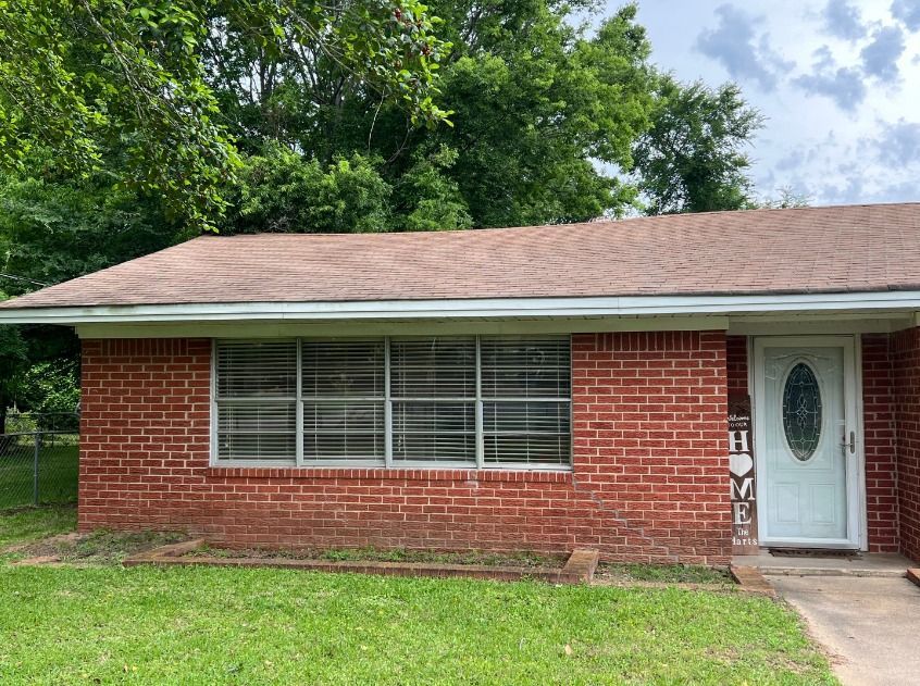 A red brick house with a white door and a brown roof is for sale.