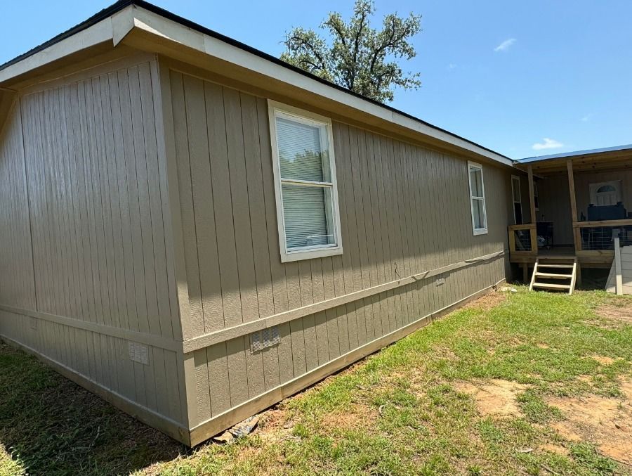 A mobile home with a porch and stairs is sitting on top of a lush green field.