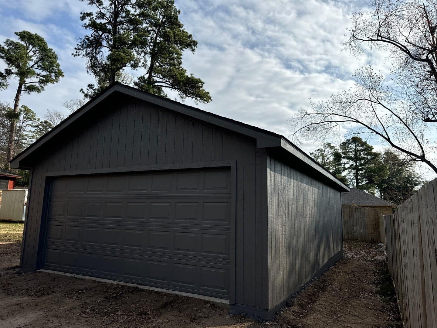 A gray garage with a black roof is sitting next to a fence.