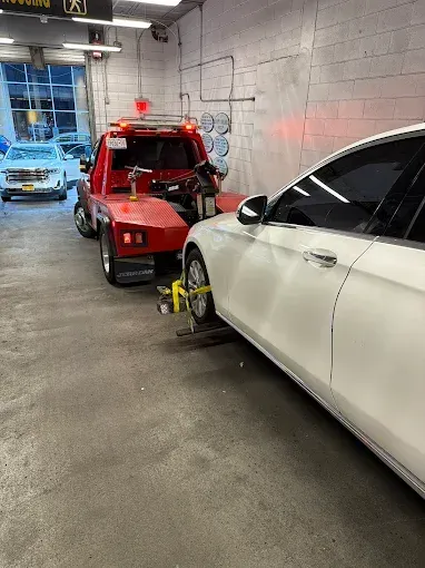 Tow truck towing a white sedan inside a garage. The truck is red; the floor is concrete.