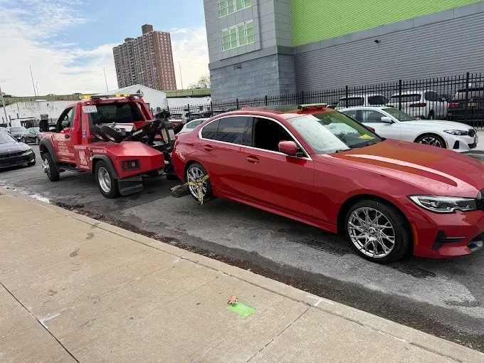 Red car being towed by a red tow truck on a city street.